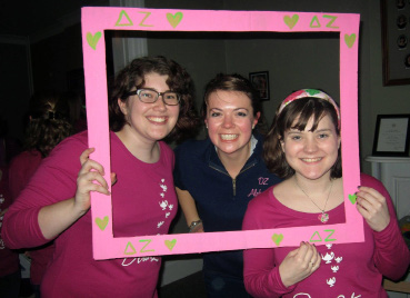 Delta Zeta women Zoe Crankshaw, Kristen Krak, and Katie Powell smile in a fake picture frame at the DZ house on Bid Day.